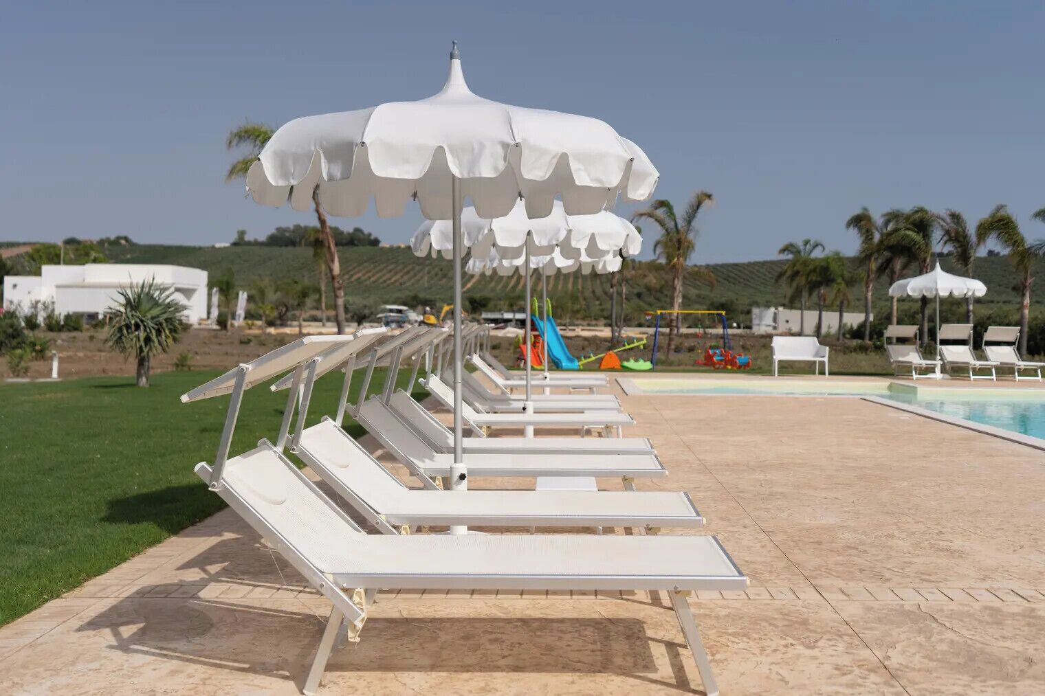 Zona de piscina con tumbonas y sombrillas blancas.