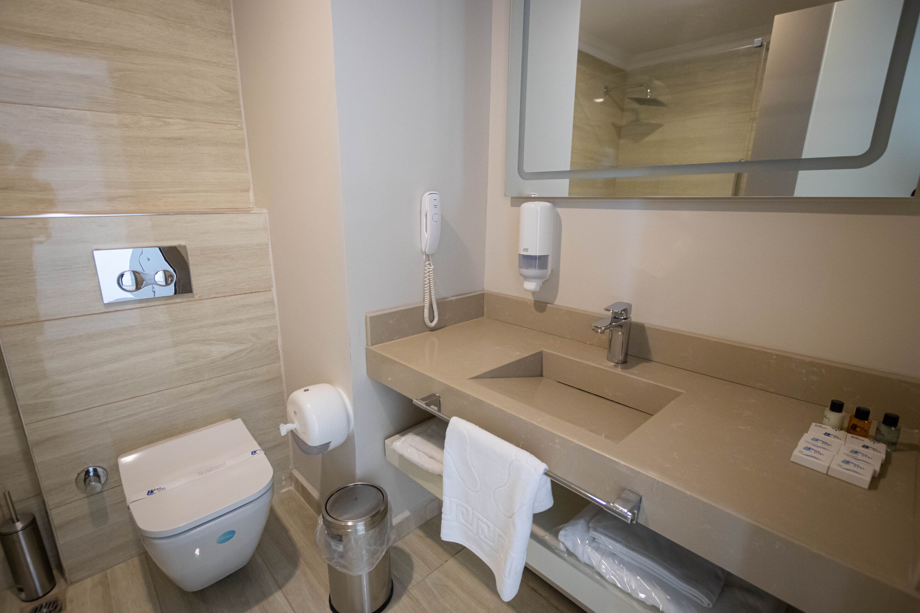 A modern bathroom with a toilet, sink, mirror, and hand dryer.