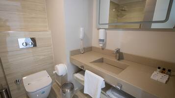 A modern bathroom with a toilet, sink, mirror, and hand dryer.