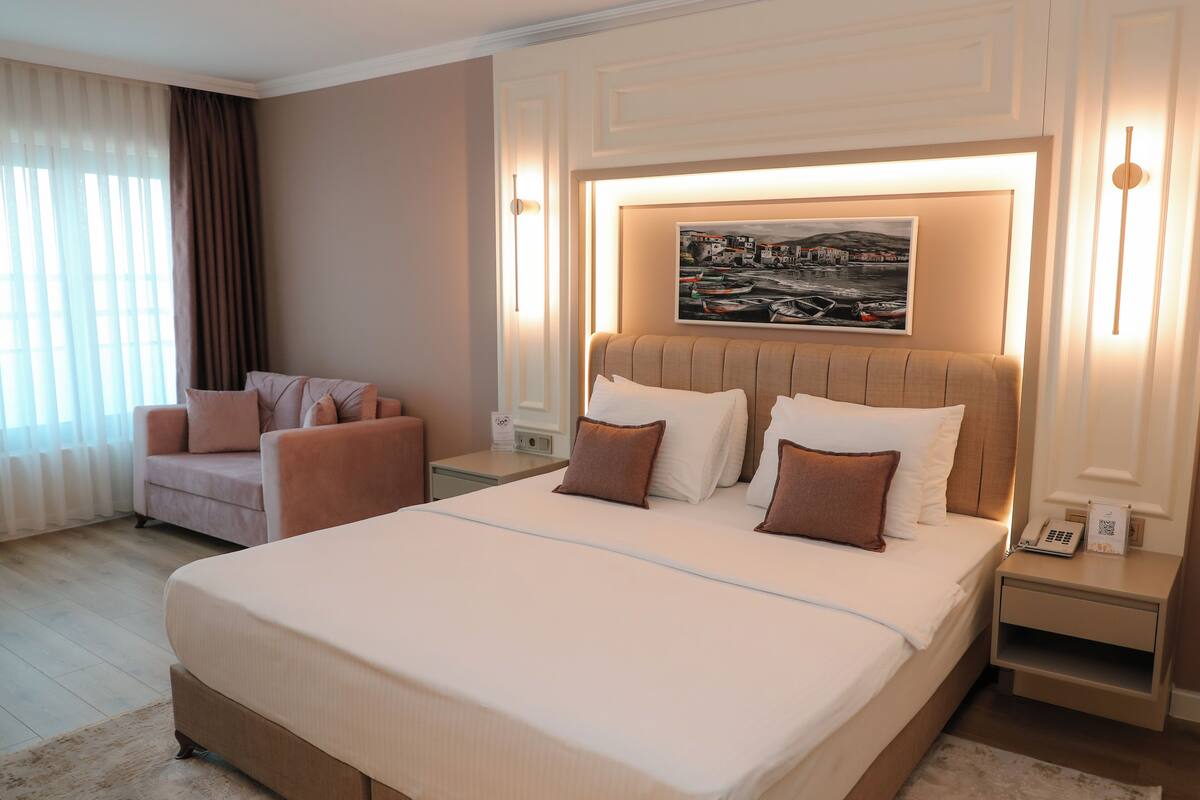 A hotel room with a large bed, a chair, a nightstand, and a painting on the wall.