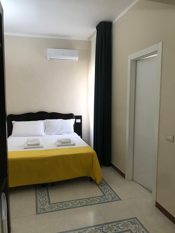 A hotel room with a bed, a door, and an air conditioning unit.