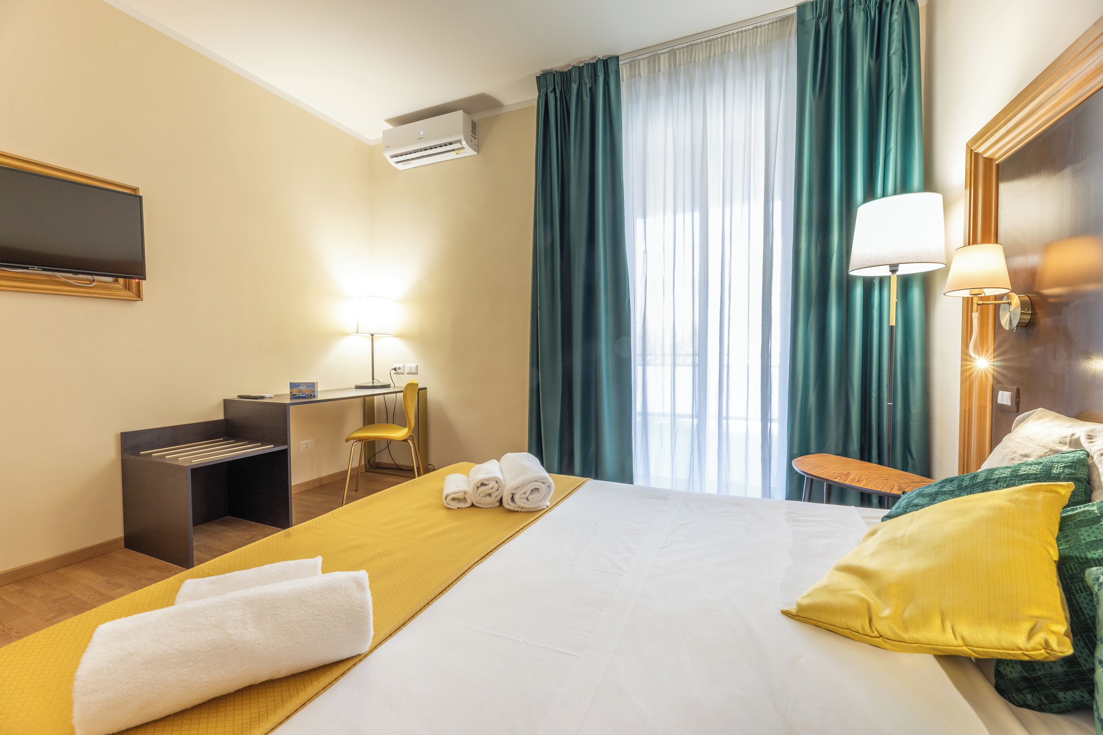 A hotel room with a bed, a desk, a chair, a TV, and a window with curtains.