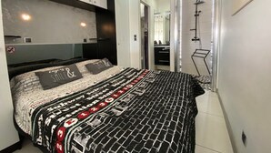 A modern bedroom with a patterned bedspread, a large mirror, and a walk-in closet. - Charming Studio, Terrace, and Parking for Two - Steps from the Beach! (Cap d'Agde naturisme)