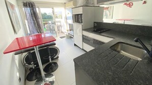 A compact kitchen with a red table, a sink, and a microwave. - Charming Studio, Terrace, and Parking for Two - Steps from the Beach! (Cap d'Agde naturisme)