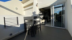A small outdoor patio area with a table and chairs, a sliding glass door leading to a covered space, and a white wall with a window. - Charming Studio, Terrace, and Parking for Two - Steps from the Beach! (Cap d'Agde naturisme)