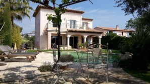 Una casa de dos pisos con piscina, mobiliario exterior y jardín.