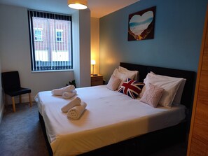 A neatly made bed with rolled towels, a British flag pillow, and a heart-shaped picture on the wall. - Station Apartment in Norwich (Norwich)