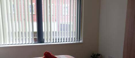 Ein Schlafzimmer mit Bett, einem Fenster mit Jalousien, einer kleinen Pflanze und einem Kleiderschrank.