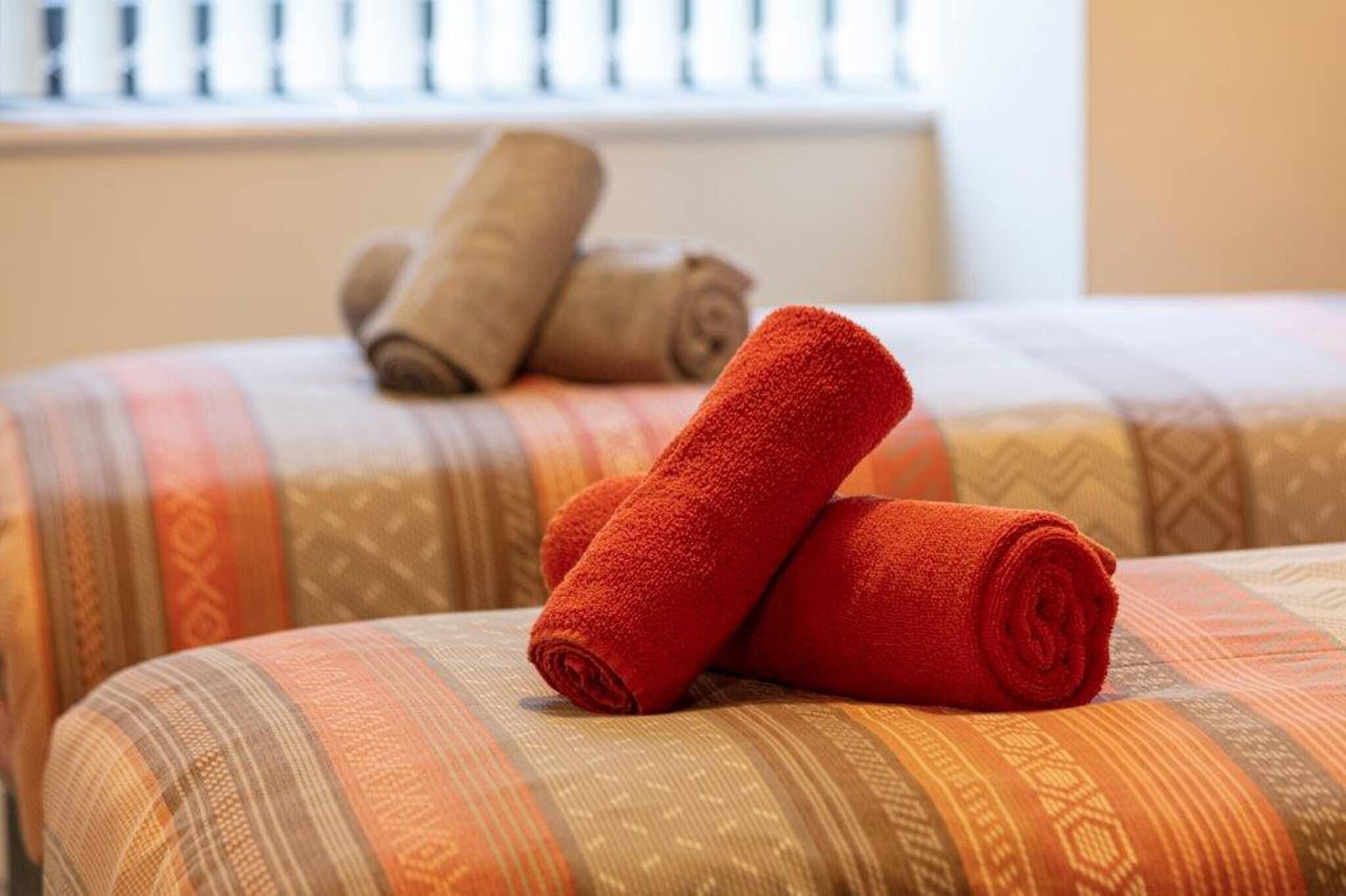 Ett hotellrum med två sängar, där varje säng har mönstrat sänglinne och hoprullade handdukar.