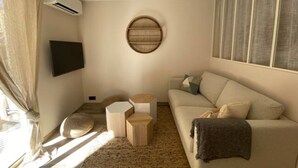 Un salon avec un canapé beige, un élément de décoration murale rond, un téléviseur à écran plat et une petite table d’appoint en bois.