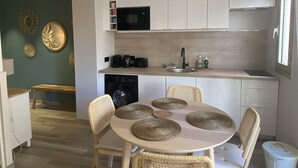 Une cuisine moderne avec des armoires blanches, un four à micro-ondes encastré et un évier. On y trouve également un coin repas avec une table ronde et des chaises en osier.