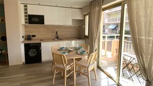Une cuisine compacte avec un coin repas, des appareils électroménagers intégrés et une porte-fenêtre coulissante donnant sur un balcon.
