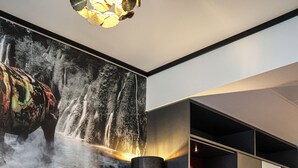 Een modern interieur met een tafel met glazen blad, een rode stoel, een bank en een muur met een schilderij van een waterval.