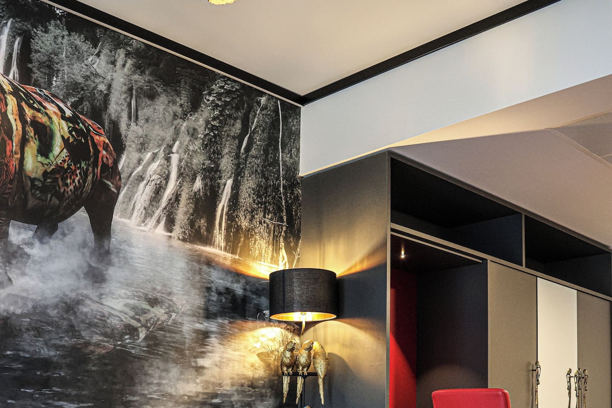 Un interior moderno con una mesa de vidrio, una silla roja, un sofá y una pared con una pintura de cascada.