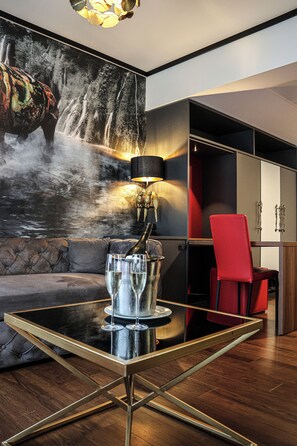 Un intérieur moderne avec une table à plateau de verre, une chaise rouge, un canapé et un mur orné d’un tableau représentant une cascade.