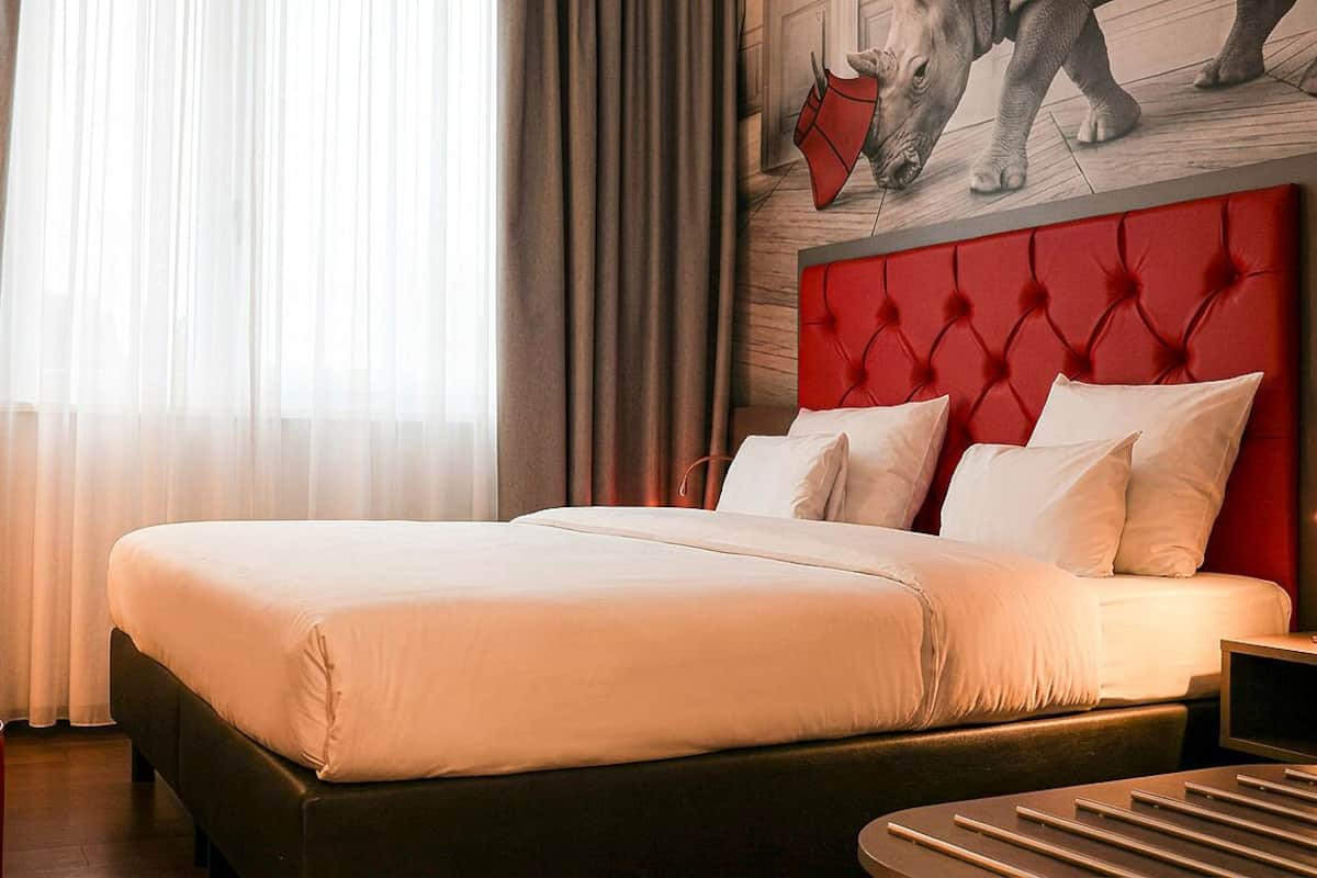 Una habitación de hotel con una cama grande, un cabecero rojo y un cuadro de un rinoceronte en la pared.