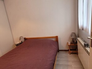 Ett litet, välordnat sovrum med en säng, ett sängbord med en lampa och en liten hylla med en vattenkokare.