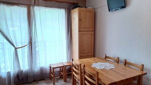A room with a wooden dining table, chairs, a television mounted on the wall, and a window with sheer curtains. - 2 rooms + cabin with balcony and equipped kitchenette (Le Biot)
