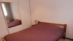 A single bed with a wooden frame and a red mattress in a room with white walls and a wooden floor. - 2 rooms + cabin with balcony and equipped kitchenette (Le Biot)