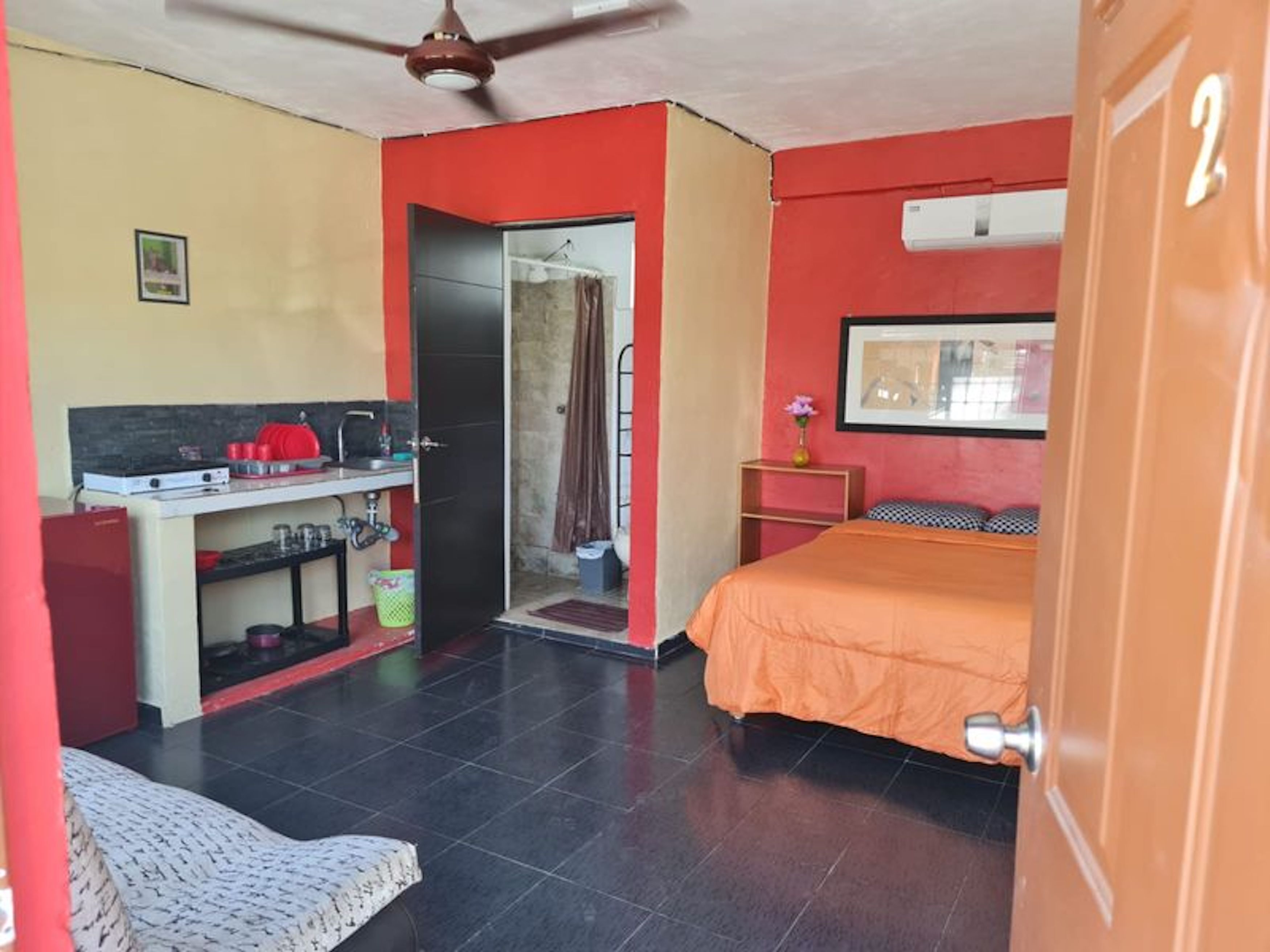 Habitación pequeña con kitchenette, una cama y zona de ducha.