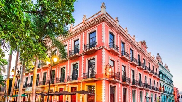 A multi-story building with balconies and large windows, surrounded by trees and street lamps. - Super Cheap Loft Style Apartment in Merida Wifi Smartv (Mérida)