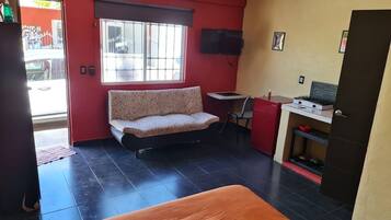 Una habitación compacta con sofá, una mesita, televisor y kitchenette.