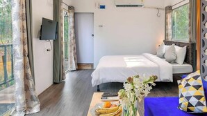 Un dormitorio con cama, televisor, ventana y una mesa con frutas y flores.