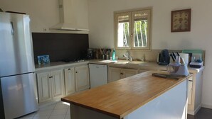 Eine moderne Küche mit weißen Schränken, einem Edelstahlkühlschrank, einer Holz Arbeitsplatte und einem Fenster mit Jalousien.