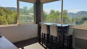 Ein Essbereich mit Tisch und Stühlen, große Fenster mit Blick auf grüne Hügel und Bäume.