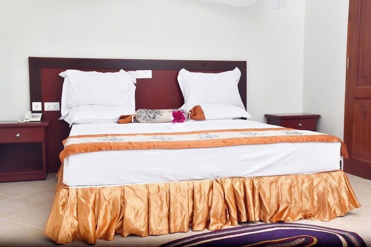 A neatly made bed with a headboard, a bedside table with a lamp, and a wall socket.