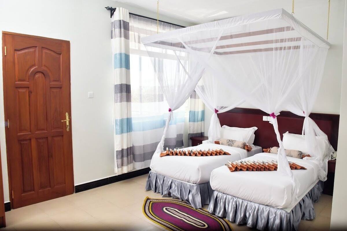 A room with two beds, a wooden door, and a striped curtain.