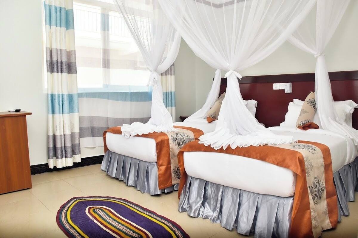 A double bed with a canopy, a bedside table, a striped curtain, and a patterned rug.