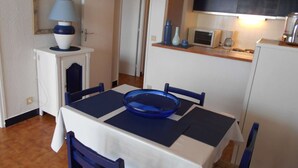 Une cuisine compacte équipée d’un four à micro-ondes, d’un grille-pain et d’une machine à café. Une table à manger avec des chaises est placée devant la cuisine.