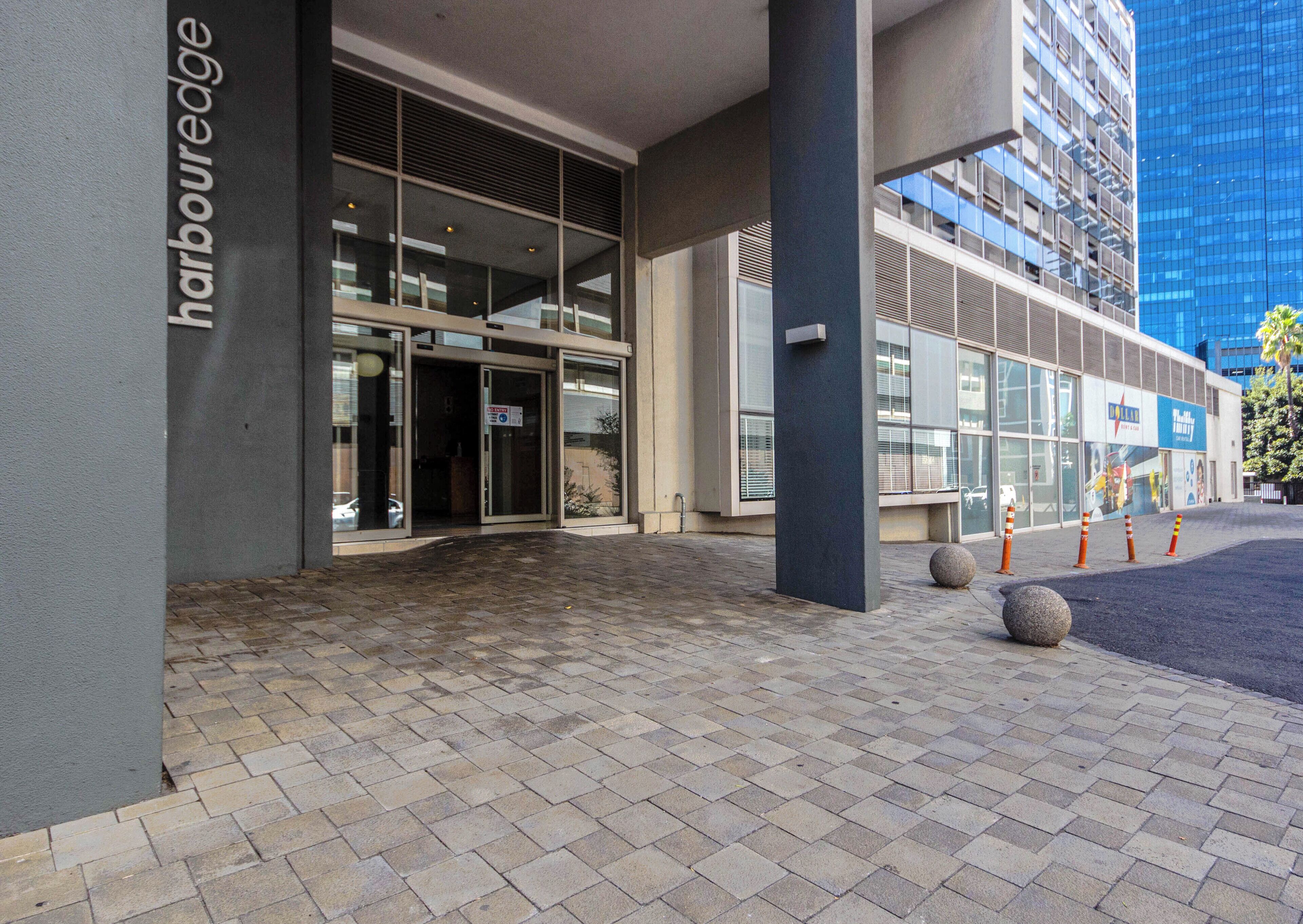 Een moderne gevel met glazen façade, een naambordje met de tekst 'harbouredge' en een verharde looppad.
