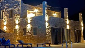 A stone building with a swimming pool, lounge chairs, and a person sitting on one of the chairs. - Luxury Villa With Private Pool Kika Residences (West Mani)