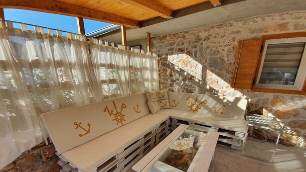 Une pièce chaleureuse avec un plafond en bois, un mur en pierre, un banc rembourré orné de motifs d’ancres et une petite table avec un plateau en verre.