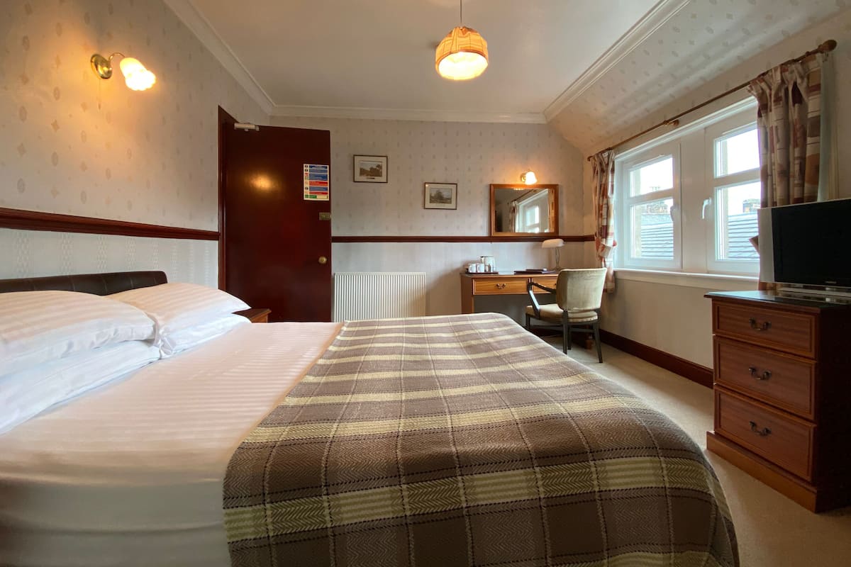 A hotel room with a bed, a desk, a chair, a dresser, and a television.