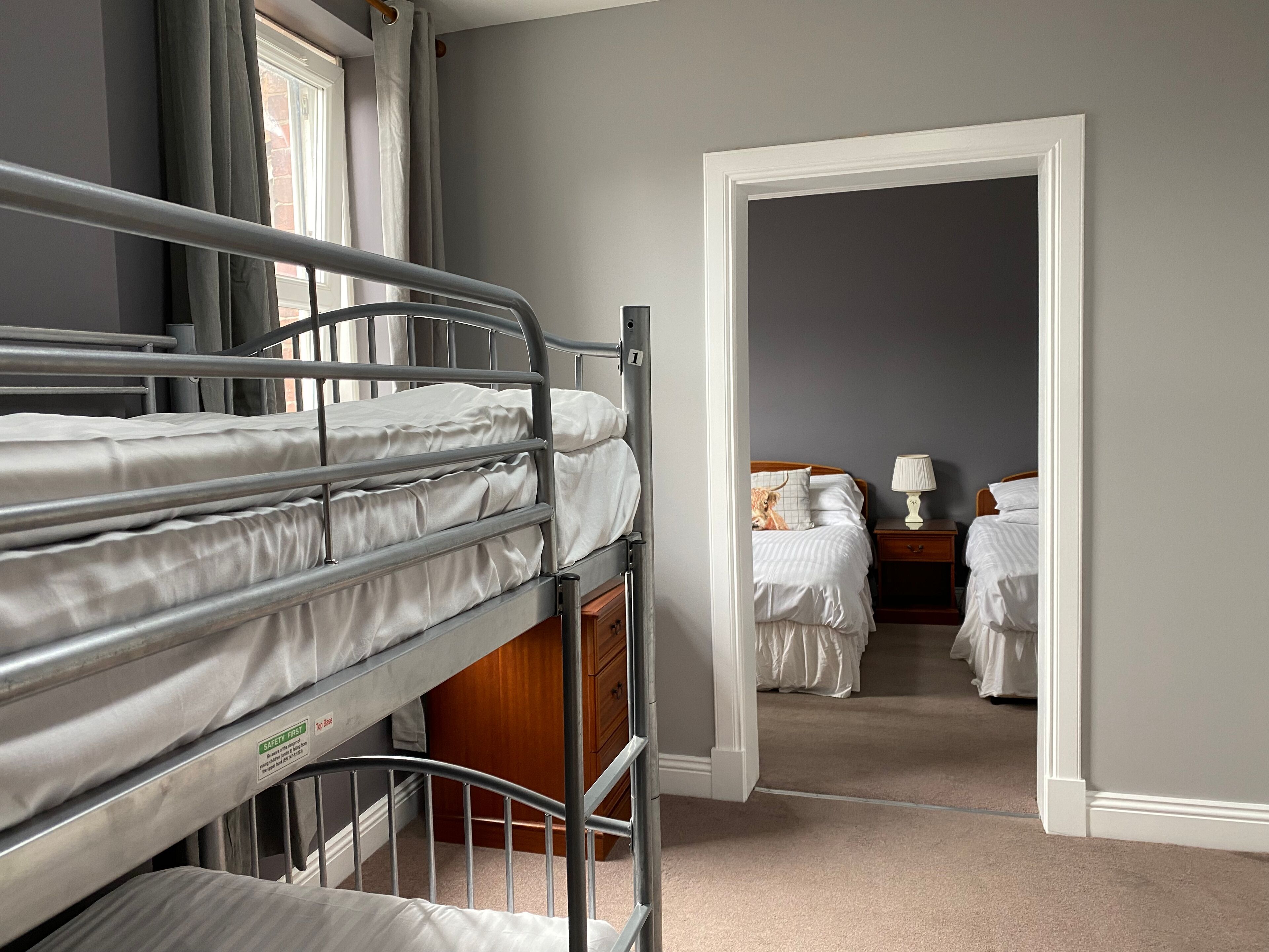 A room with bunk beds, a wooden wardrobe, a nightstand with a lamp, and a bed with a lamp.