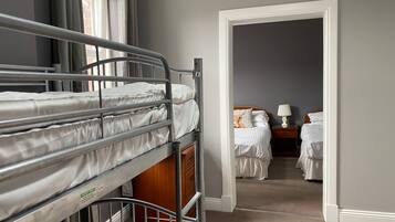 A room with bunk beds, a wooden wardrobe, a nightstand with a lamp, and a bed with a lamp.