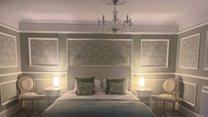 A bedroom with a large bed, two bedside tables with lamps, a chandelier, and floral wallpaper. - The Kings Arms Hotel (Lockerbie)