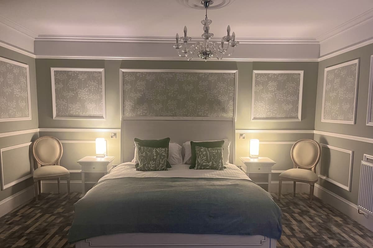 A bedroom with a large bed, two bedside tables with lamps, a chandelier, and floral wallpaper.