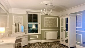 A room with a patterned floor, a white dresser, a mirror, a radiator, and a chandelier. - The Kings Arms Hotel (Lockerbie)
