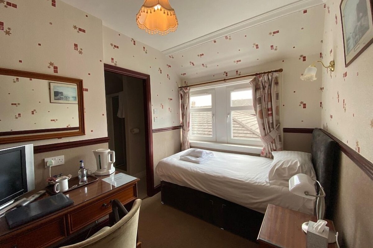 A hotel room with a bed, desk, chair, and a television.