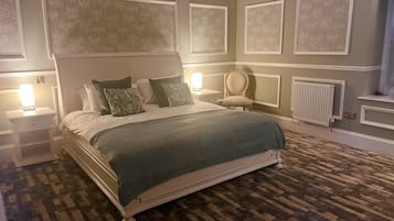 Un dormitorio ordenado con una cama grande, una silla y una mesita de noche con lámpara.
