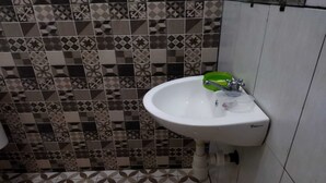 Ein Badezimmer mit einem weißen Waschbecken, einem grünen Seifenspender und gemusterten Fliesen an Wänden und Boden.