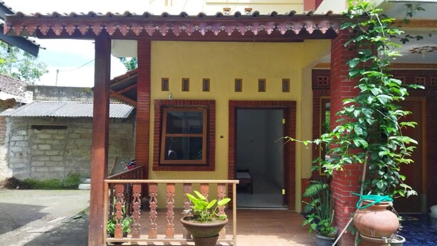 Ein Haus mit gelber Fassade, einer Holzveranda mit Geländer und einem Blumentopf im Vordergrund.