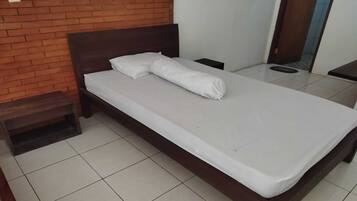 A neatly made bed with white linens in a room with a tiled floor and a brick wall.