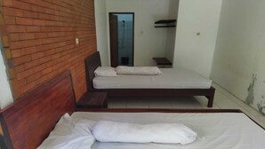 Ein Zimmer mit zwei Betten, einem Holzkopfende, einer Ziegelwand und einem kleinen Badezimmer mit Dusche.