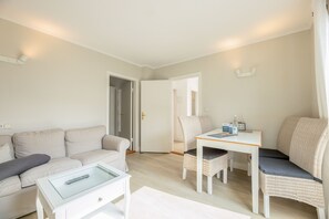 Un salon comprenant un canapé, une table basse, une table à manger avec des chaises et une porte donnant sur une autre pièce.
