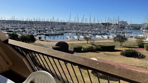 A marina with numerous boats docked, a clear sky, and a balcony with a chair and railing.